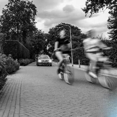2 fietsers op de voorgrond, ver in de straat een auto